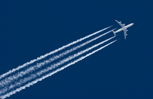 A distant passenger jet flies out from behind a cloud