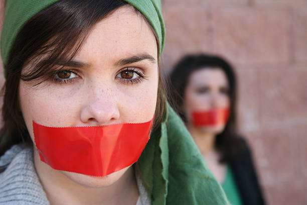 Woman Wearring A Head Scarf With Red Tape On Mouth A girl with red tape over her mouth. Copy space on the right. strike protest action photos stock pictures, royalty-free photos & images