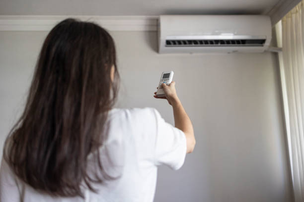istock Caucasian woman turning on air conditioner with remote control 1574002249