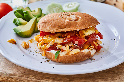 A healthy scrambled eggs protein burger with cherry tomatoes, avocado, cucumber, fresh seasoning herbs and spices, representing a fit lifestyle, wellbeing and a citylife. Side view image