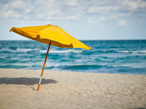 Child in sun hat, under a sun umbrella, looking out to sea, Omaha Beach, Auckland, New Zealand, summer holiday