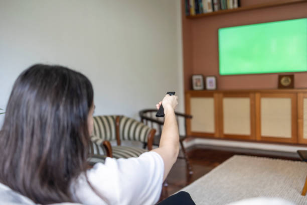 istock Woman turning on the tv by remote control 1574004349