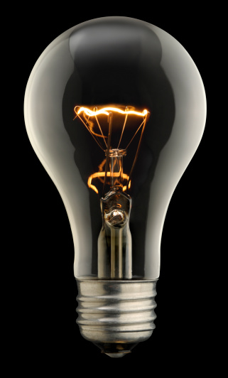 A classic lightbulb hovering over a dark surface, the filament is glowing - concept for having an idea, innovation
