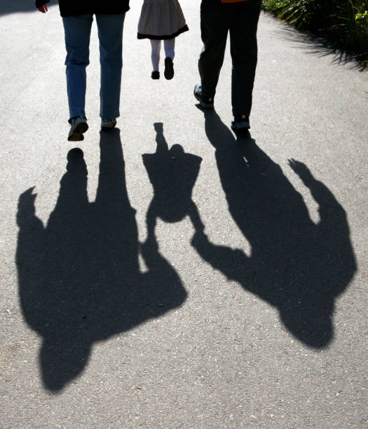 shadows of parents lifting child shadows behind two adults carrying a child on a sidewalk family shadow stock pictures, royalty-free photos & images
