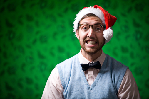 A cheesy faced nerd young man wearing a Santa Claus hat at Christmas time.  Horizontal with copy space.