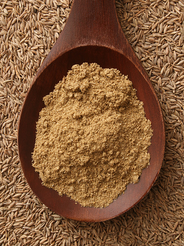 Top view of wooden spoon with ground cumin on it