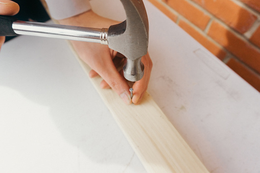 Close up of a person hammering a nail into a plank of wood