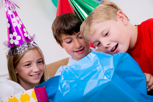 A group of children opening presents at a birthday party.