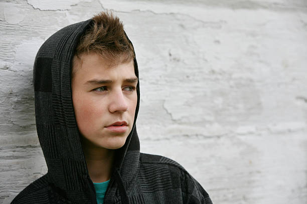 teen boy with hoodie in front of old white wall - achterdocht fotos stockfoto's en -beelden