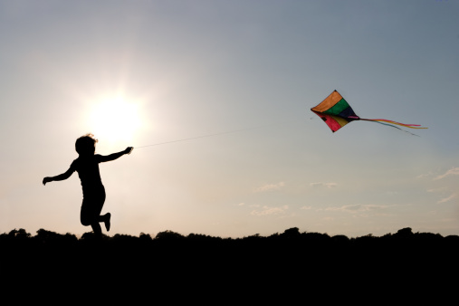 A silhouette of a child running and flying a kite.