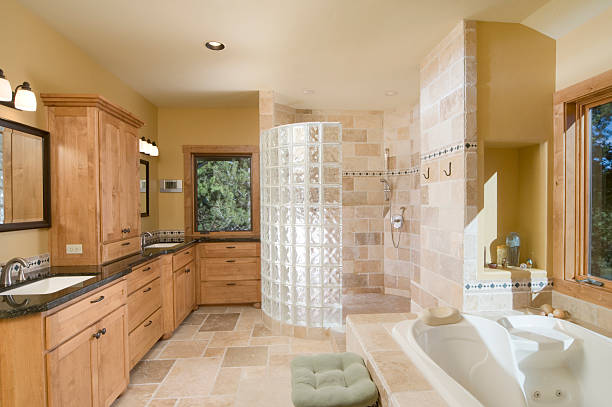 A bathroom with a white cabinet and countertop, glass block window, and a shower with brown tiles.