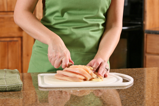 Slicing raw chicken and other ingredients for a meal.