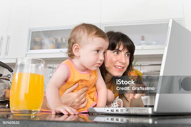 Baby With Mother At The Laptop In Kitchen Stock Photo - Download Image Now - 12-17 Months, 12-23 Months, 25-29 Years