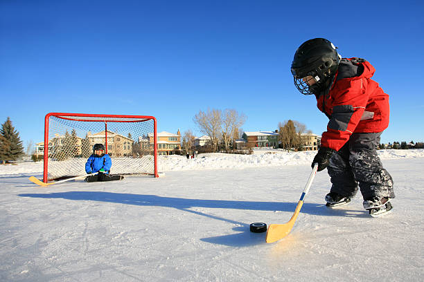 enfants jouant au hockey sur glace sur patinoire extérieure et un étang - ice hockey child childhood little boys photos et images de collection