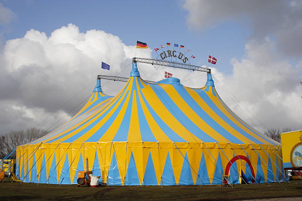 Yellow and light blue circus tent over a cloudy sky Focus on the blue and yellow Circus tent in windy weather! circus photos stock pictures, royalty-free photos & images