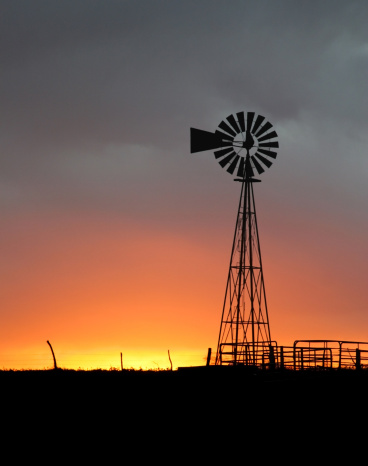sunset over the western kansas prairie with windmill silouette, cattle pen and fence in foreground; room for text