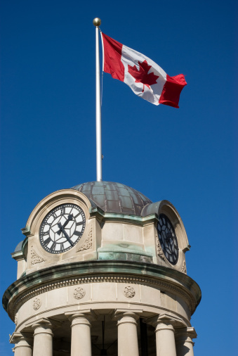 The clock tower in Kitchener's Victoria Park with the Canadian Flag against a brilliant blue sky.