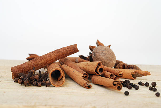 Aromatic Spices on a Wooden Cutting Board with a White Background A loose pile of cinnamon sticks, whole cloves, cardamon, black pepper corns, whole nutmeg, and star anise on wood, with a white background.  Warm tones of brown and orange. nutmeg stock pictures, royalty-free photos & images