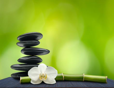 Balanced Spa Stones, Orchid Flower and Bamboo on Black Mat with Soft Green Background.