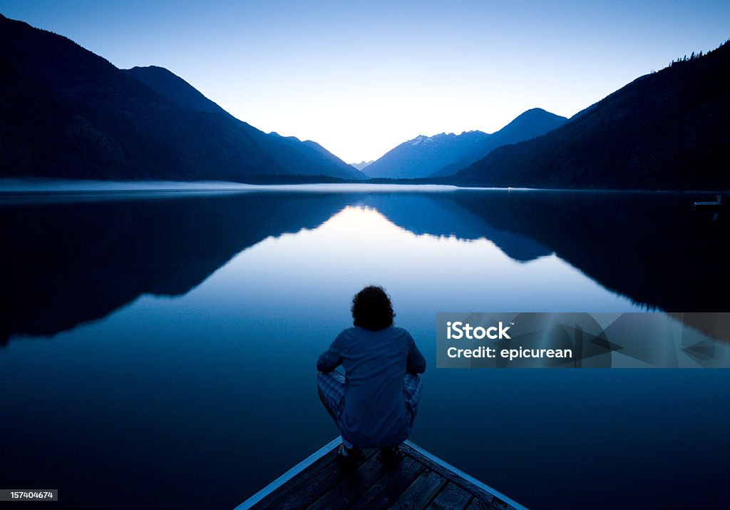 The World at Rest Person sitting quietly on the edge of a dock watching the sunset Contemplation Stock Photo
