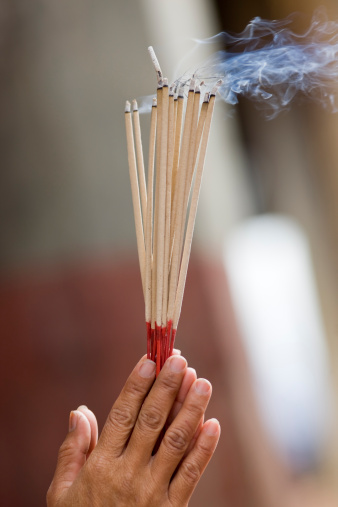 Paying homage, with burning incense sticks at a Buddhist temple in Thailand. Selective focus on the hands. 
