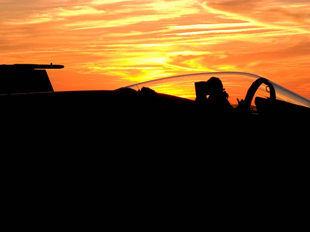 Shown here is an F,A-18 Hornet sitting on the flight deck of an aircraft carrier surrounded by a brilliant sunset The pilot is signaling thumbs up No visible ID markings.