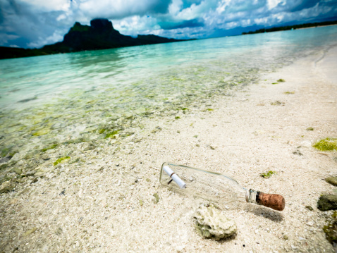 Message in a bottle stranded at the beach of Bora Bora Island. Volcanic Mountain in the background. Bora Bora Lagoon, Society Islands, French Polynesia.