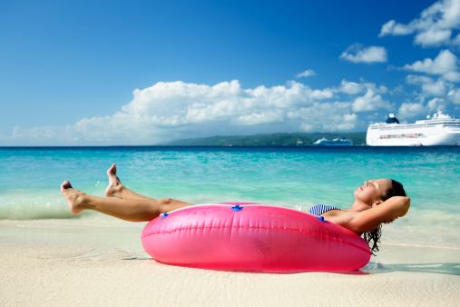 woman relaxing in raft on a beach with cruise ship in the background