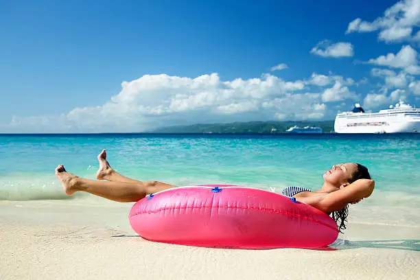 woman relaxing in raft on a beach with cruise ship in the background