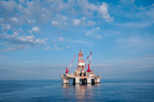 A deep water oil drilling platform at sea with calm waters and cumulus clouds against blue sky. 