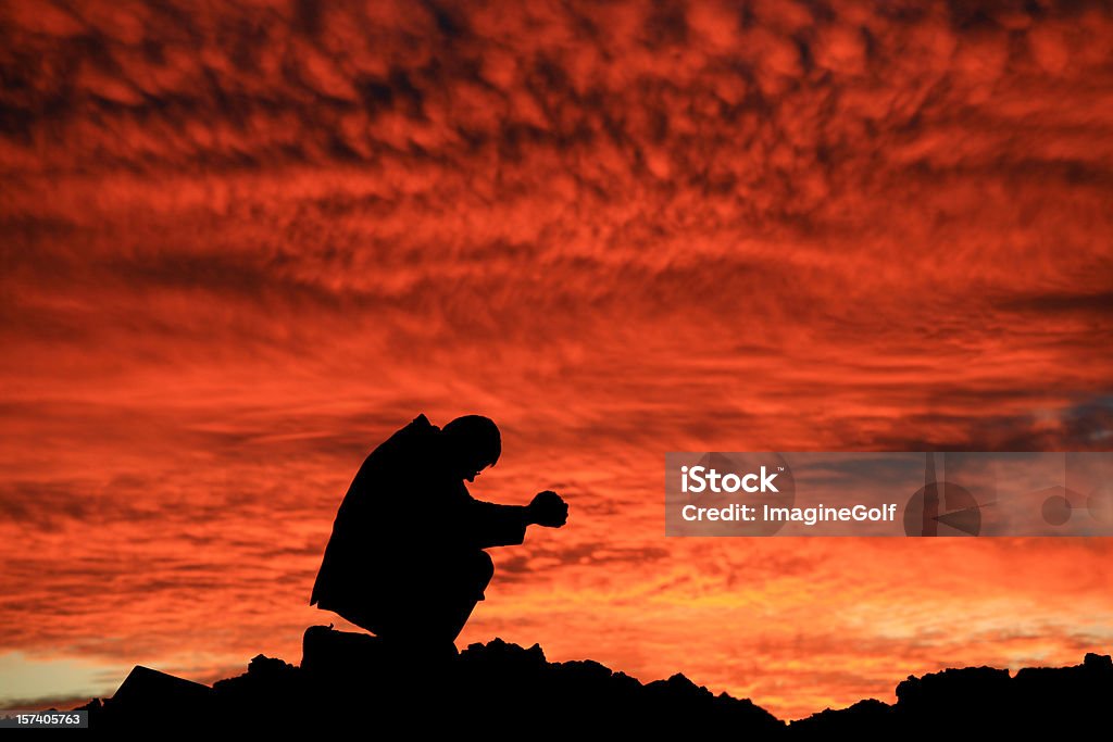 Businessman Saying a Prayer at Sunset Silhouette A businessman prays against dramatic sunset. No colour manipulation. Just one of the best sunsets I've ever seen! Additional themes in the image include business, future, hope, hurting, pain, prayer, meditation, downfall, collapse, gratitude, forgiveness, salvation, faith, god, depression, sadness, confusion, spirituality, balance, Christianity, religious, bowing, kneeling, hands folded, and unrecognizable male in his 30s.  Adult Stock Photo