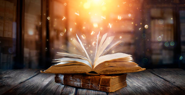 Old Book With Magic Lights And Bright Letters On Aged Table In Defocused Library stock photo