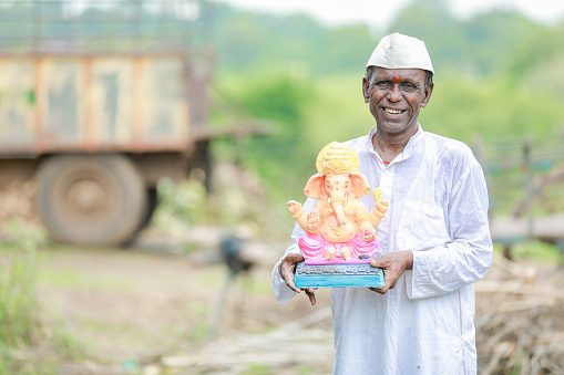Indian old man holding Lord Ganesha idol in hands , happy old poor man