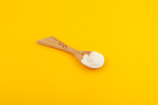 Guar gum powder or guaran in wooden spoo on yellow background, selective focus. Design element. Food additive E412. Thickening agent. Stabilizer and Fat Replacer.