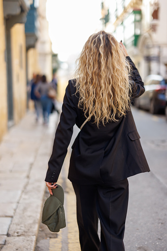 Back view of fashionable young woman walking in the city