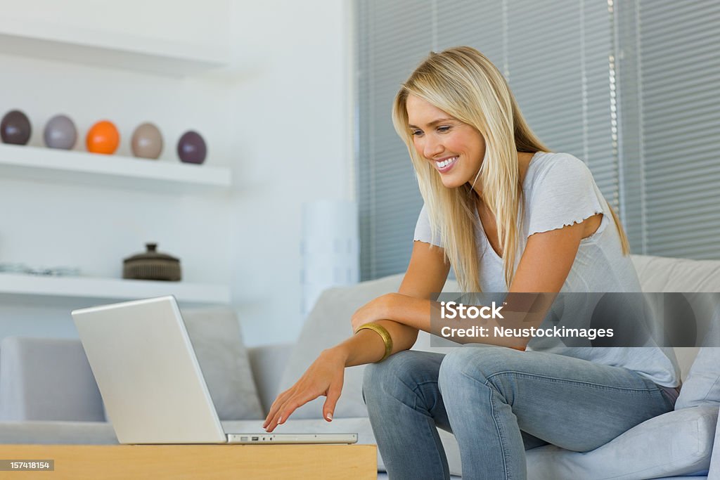 Sonriente Joven mujer sentada frente a la computadora portátil - Foto de stock de Delante de libre de derechos