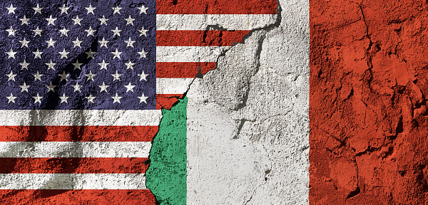 Cooperation or conflict? National flags of the United States and Italy on a cracked, textured plastered wall, representing diplomacy, trade or geopolitics.