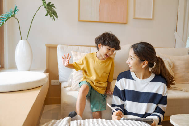 Single mother spending time with her son while staying at home. Asian mother teaching her naughty son to draw pictures on a digital tablet while staying at home. asian nanny stock pictures, royalty-free photos & images