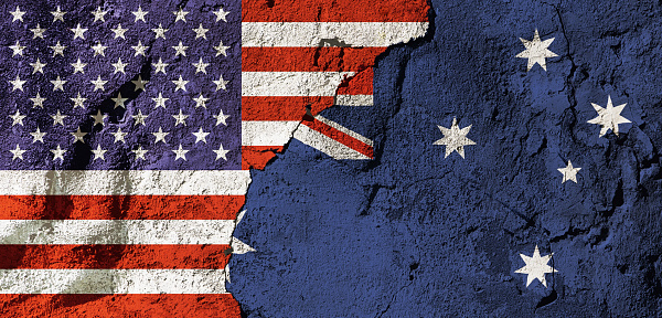 Cooperation or conflict? National flags of the United States and Australia on a cracked, textured plastered wall, representing diplomacy, trade or geopolitics.