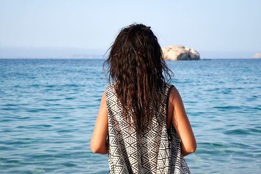 A woman leisurely strolling on a picturesque beach, with the crystal blue ocean in the background