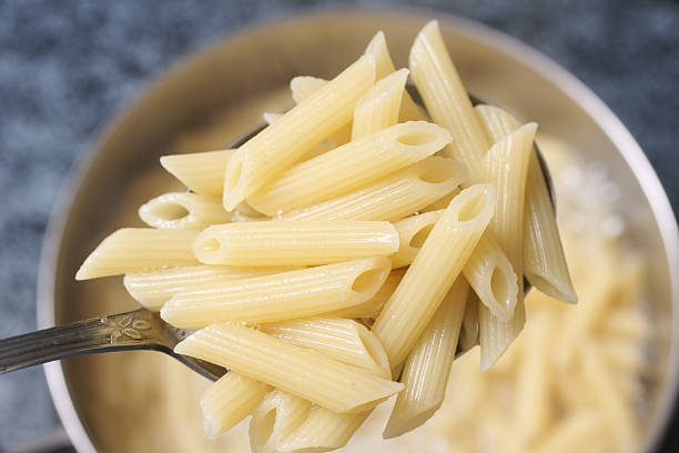 cooked penne rigate pasta in spoon - koperen pan stockfoto's en -beelden