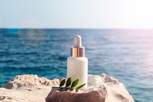 Cosmetic serum bottle on stone on the background blue sea in sunlight, closeup.