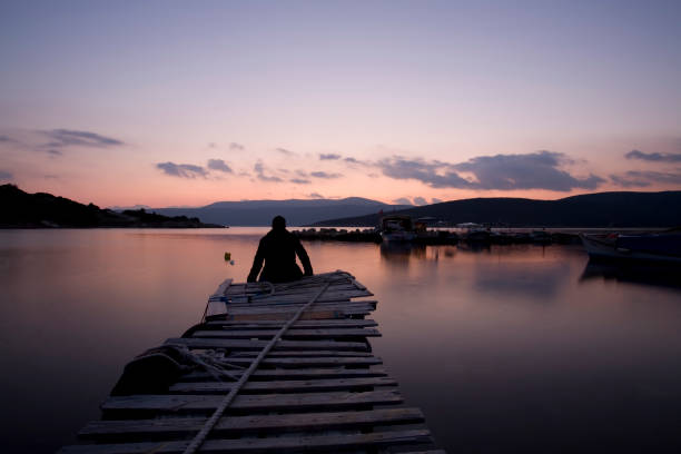 silhouette of a seated male photographer with his camera at his side watching the sunset on the lake