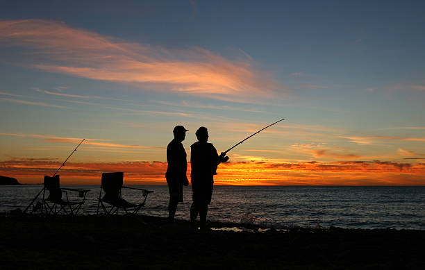 Silhouettes fishing on the beach stock photo