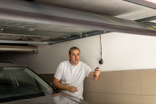 Man opening door in a garage with remote control, standing beside his car