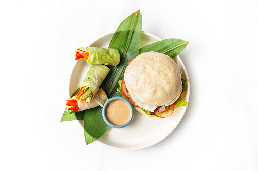 Burger with Bao steamed buns, spring rolls and sesame sauce on the plate isolated