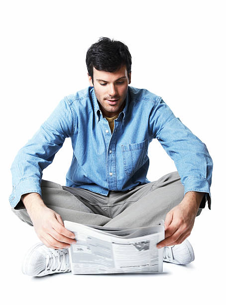 Young man sitting on the floor reading newspaper