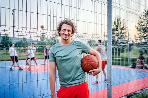 Cheerful young man with a basketball standing in front of a basketball court