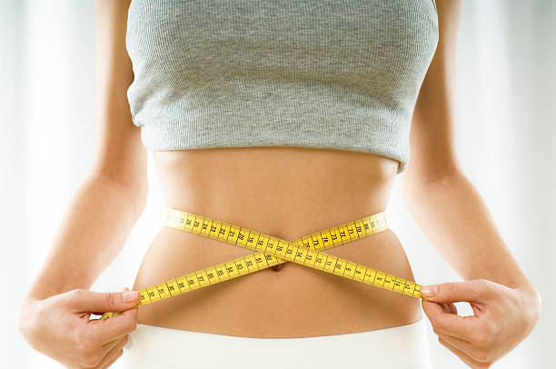 Mid section view of a young woman measuring her waist mid section view of a woman measuring her waist diets stock pictures, royalty-free photos & images