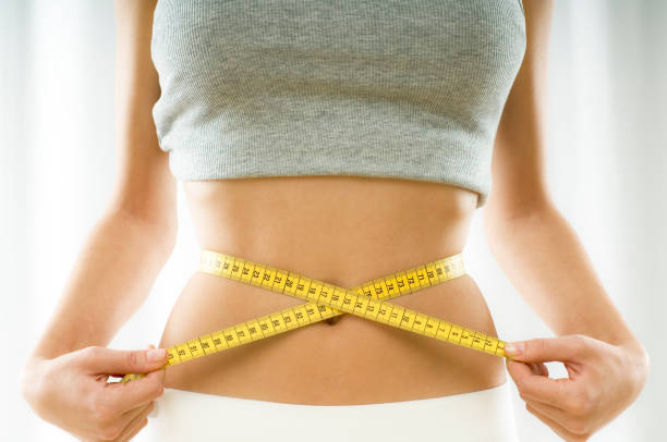 Mid section view of a young woman measuring her waist mid section view of a woman measuring her waist dieting stock pictures, royalty-free photos & images